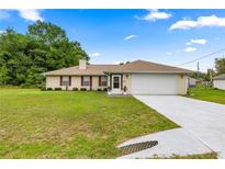 Inviting single-story home featuring a well-manicured lawn and neutral exterior with red shutters and a two-car garage at 12 Hemlock Radial Pass, Ocala, FL 34472