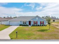 Charming single-story home with a well-manicured lawn, attached garage, and inviting red door at 3418 Sw 155Th Pl, Ocala, FL 34473