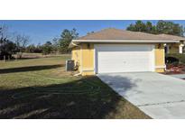 Two car garage with a large driveway and green yard around a yellow home at 360 Marion Oaks Golf Way, Ocala, FL 34473