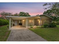 Charming single-story home with a carport, screened porch, and well-maintained landscaping under a colorful sky at 10012 Sw 88Th Ct, Ocala, FL 34481