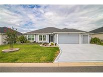 Charming single-story home featuring a well-manicured lawn, colorful landscaping, and a two-car garage at 6877 Minchew Cir, The Villages, FL 34762