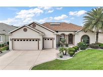 Charming stucco home with a three-car garage, well-manicured lawn, and lovely landscaping at 12169 Se 172Nd Ln, Summerfield, FL 34491