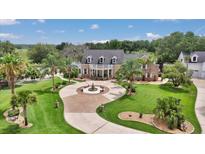 Stunning brick home featuring manicured lawn, circular drive with fountain, and lush tropical landscaping at 4550 County Road 104, Oxford, FL 34484