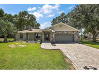 Charming single-story home featuring a stone-accented facade, paver driveway, and beautifully landscaped front yard at 15360 Se 73Rd Avenue, Summerfield, FL 34491