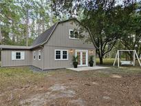 Charming gambrel house with double doors, white trim, front patio, and complemented by lush greenery and a swing at 9805 Se 182Nd Avenue Rd, Ocklawaha, FL 32179
