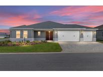 Beautiful single-story home featuring a three-car garage, well-manicured lawn, and paver driveway under a colorful sunset at 10008 Sw 85Th Place Rd, Ocala, FL 34481