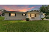 Charming single-story home featuring a cozy front porch and well-maintained lawn at sunset at 10720 Sw 63Rd Ave, Ocala, FL 34476