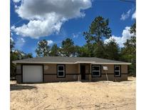 Single-story home boasts a classic design with a single-car garage and neutral color palette, set against a sunny sky at 21712 Sw Rainbow Lakes Blvd, Dunnellon, FL 34431