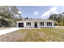 Charming single-story home featuring a modern exterior, a dark one-car garage, and a well-manicured front lawn at 23995 Nw Falcon Ave, Dunnellon, FL 34431