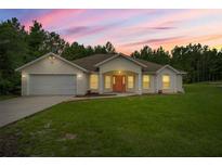 Charming single-story home featuring a manicured lawn, a two-car garage, and a welcoming coral-colored front door at 144 Malauka Pass, Ocklawaha, FL 32179