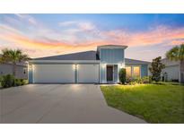 Charming light blue home boasting a well-manicured lawn and a spacious three-car garage, bathed in the warm glow of the sunset at 9209 Sw 58Th Cir, Ocala, FL 34476