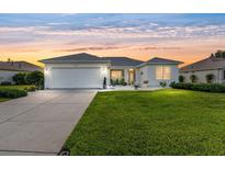 Charming one-story home featuring a manicured lawn, a two-car garage, and beautiful landscaping at sunset at 12489 Se 90Th Ter, Summerfield, FL 34491