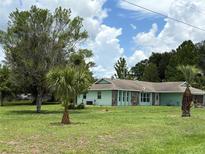 Charming single-story home with light green paint and stone accents sits on a lush green lawn with mature trees at 6773 Se 87Th St, Ocala, FL 34472