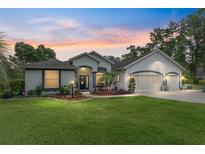 Charming one-story home with a well-manicured lawn and a three car garage, illuminated by twilight at 19115 Sw 98Th Loop, Dunnellon, FL 34432