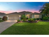 Stunning home exterior featuring lush landscaping, paver driveway and warm exterior lighting at dusk at 3001 Hillside Ln, The Villages, FL 32162
