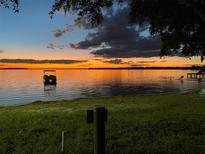 Beautiful waterfront sunset view overlooking the water, dock, and grassy lawn at 253 Blackwell Villa Cv, Babson Park, FL 33827