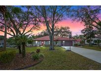 Charming home with a red-tiled roof, manicured lawn, mature trees, and inviting sunset sky at 128 Lake Ring Dr, Winter Haven, FL 33884