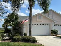 Charming home with a two-car garage, an American flag, and tropical landscaping including mature palm trees at 37 Enclave Dr, Winter Haven, FL 33884