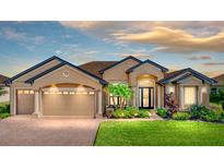 Charming tan home features a three-car garage, beautiful landscaping, brick driveway and walkway at 1336 Oakmont Dr, Winter Haven, FL 33884