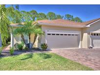 Beige single-Gathering home with a two-car garage, brick paver driveway, and tropical landscaping at 1573 Vienna Square Dr, Winter Haven, FL 33884