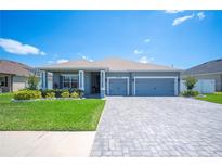 Charming single-story home with a well-manicured lawn, paver driveway, and a two-car garage under a clear blue sky at 157 Walkers Point Dr, Auburndale, FL 33823