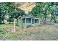 Charming, light-green cottage-style home with a screened-in porch, surrounded by mature trees and a cloudy sky at 230 Denton Ave, Auburndale, FL 33823