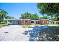 Charming brick home featuring a covered carport, mature trees, and a welcoming driveway at 961 Oleander Se Dr, Winter Haven, FL 33880