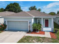 Charming single-story home featuring an attached two-car garage, red door, landscaped front yard, and mature trees at 481 Kensington View Dr, Winter Haven, FL 33880