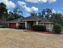 Inviting single-story home featuring a red door and garage door, enhanced by lush landscaping and mulch at 7741 Merrily Way, Lakeland, FL 33809
