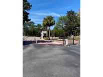 View of a gated entrance with a guardhouse surrounded by trees and blue sky at 1134 S Pine Ridge Cir # 34, Sanford, FL 32773