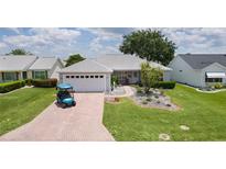 Charming single-story home with a well-manicured lawn, paver driveway, and a blue golf cart at 1305 Guerra Ave, The Villages, FL 32159