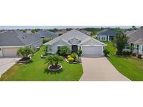 Landscaped front yard featuring lush lawn, decorative trees and shrubbery leading to a gray home with a two car garage at 924 Figwood Loop, The Villages, FL 32163