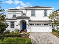 Beautiful two-story home featuring a well-manicured lawn, a paver driveway, and a covered entrance with a blue front door at 9099 Hazard St, Davenport, FL 33896