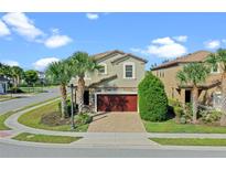 Charming two-story home with well-maintained landscaping, palm trees, a brick driveway, and a red garage door at 5569 Misty Oak Cir, Davenport, FL 33837