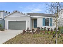 Charming single-story home featuring a grey garage door, blue door, manicured landscaping, and vibrant plants at 5410 Catmint Dr, Lake Hamilton, FL 33851