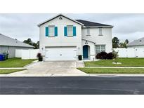 Inviting two-story home featuring a two-car garage, well-maintained lawn, and vibrant turquoise shutters and front door at 5783 Marsh Landing Dr, Winter Haven, FL 33881
