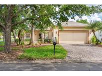 Charming single-story home with a well-manicured lawn, mature trees, and a brick driveway leading to an attached two-car garage at 753 Largo Pass, Poinciana, FL 34759