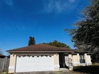 One-story house with brown roof, white garage door, and mature trees at 2704 Kendall Ave, Kissimmee, FL 34744