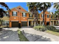 Orange townhouses with attached garages, palm trees, and lush landscaping at 904 Assembly Ct, Reunion, FL 34747