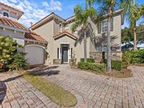 Tan two-story home with tile roof, paver driveway, and lush landscaping at 220 Brunello Dr, Davenport, FL 33897