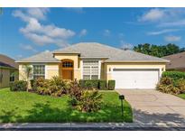 Beautiful yellow house with a gray roof, white garage door, and lush landscaping at 135 Langham Dr, Davenport, FL 33897