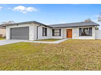 Updated single story home with gray garage door and orange front door at 202 Cobalt Dr, Kissimmee, FL 34758