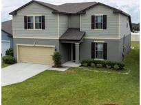 Two-story home featuring neutral siding, black shutters, a well-maintained lawn, and an attached two-car garage at 446 Citrus Isle Loop, Davenport, FL 33837