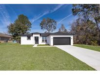 White house with black accents, concrete driveway, and grassy lawn at 4411 Sw 132Nd Pl, Ocala, FL 34473