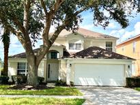 Two-story house with a large front yard, white garage door, and mature trees at 8417 Secret Key Cove, Kissimmee, FL 34747