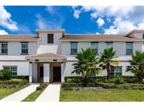 Two-story townhome with Spanish tile roofing, lush landscaping, and a walkway at 9003 Stinger Dr, Davenport, FL 33896