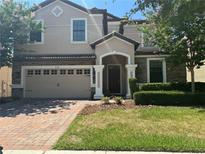 Two-story house with a beige exterior, brown accents, and a brick driveway at 9158 Scramble Dr, Davenport, FL 33896