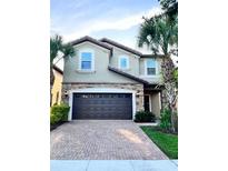 Two-story house with dark brown garage door, brick driveway, and palm trees at 2112 Morocco Way, Kissimmee, FL 34747
