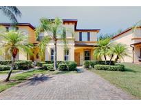 Inviting two-story townhome featuring a brick driveway and well-manicured landscaping with mature palm trees at 3939 Calabria Ave, Davenport, FL 33897