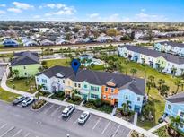 Community aerial view showcasing colorful townhomes, pool, parking, and landscaping under a clear blue sky at 2960 Caribbean Soul Dr, Kissimmee, FL 34747